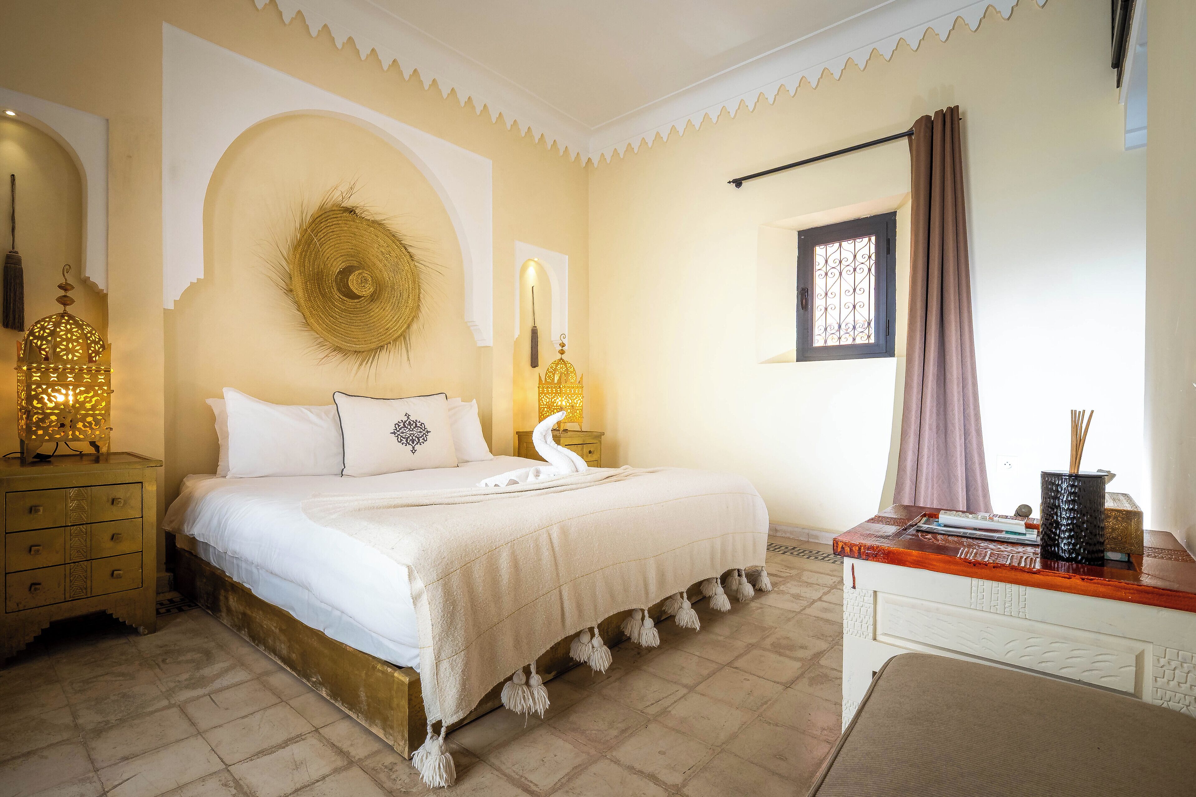 Un dormitorio con cama, mesitas de noche, escritorio y objetos decorativos.