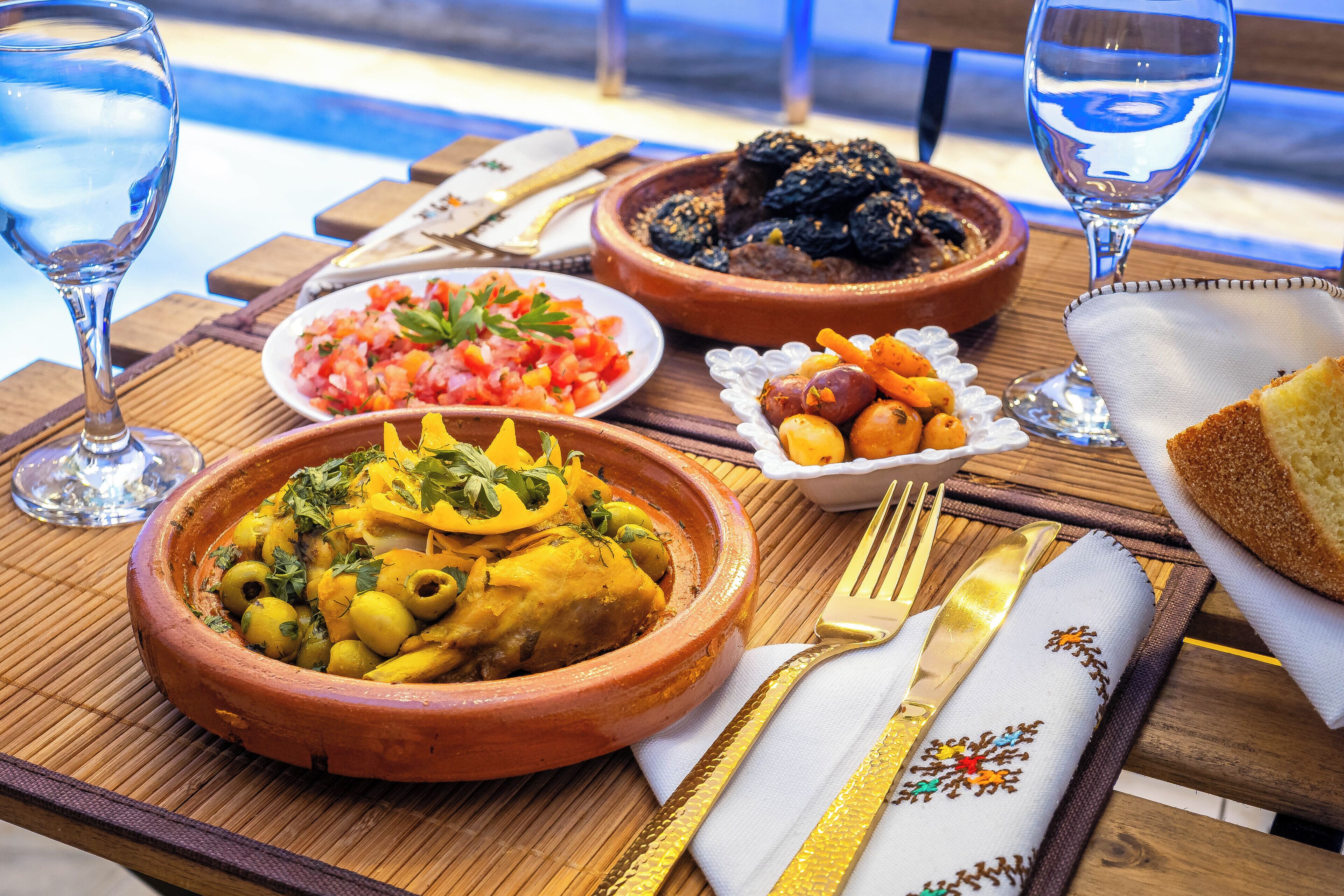Una mesa con diversos platos, incluyendo un tazón de aceitunas, un tazón de tomates, un tazón de dátiles y un plato de pan.