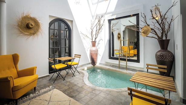 A sunlit indoor pool area with a yellow armchair, wooden table, and chairs. - Riad Come&va (Marrakech)