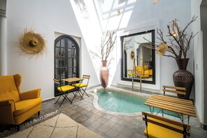 Zona interior de piscina iluminada por el sol, con un sillón amarillo, una mesa de madera y sillas.