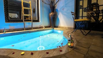 Uma piscina com pétalas de rosa e velas, uma escada, um vaso grande e um candeeiro.