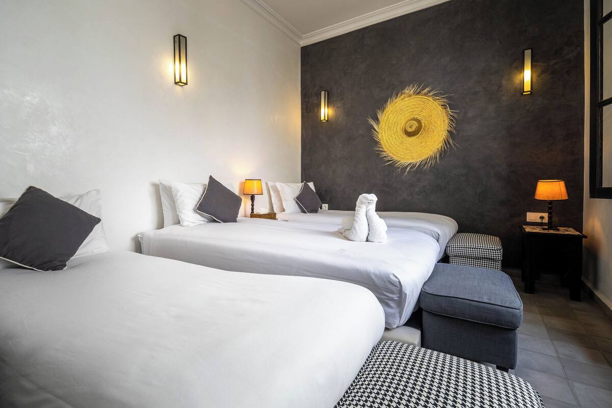 Ein Hotelzimmer mit drei Betten, einer dunkel gestrichenen Wand und einem Wandbild, das einer Sonne ähnelt.