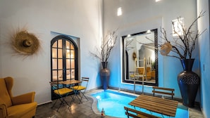 A cozy indoor pool area with a wooden bench and yellow chairs, surrounded by large vases and a rustic wall decor. - Riad Come&va (Marrakech)