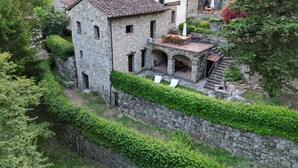 Un bâtiment en pierre doté d’une terrasse et d’arcades, entouré de verdure et de montagnes.