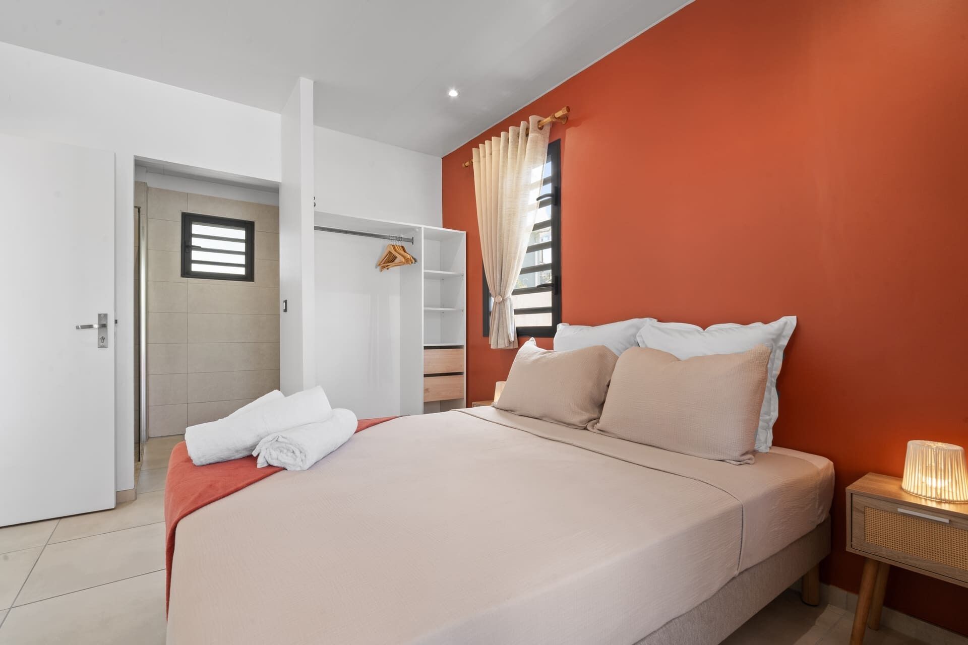 A bedroom with a bed, a nightstand, a wardrobe, and a window with curtains.