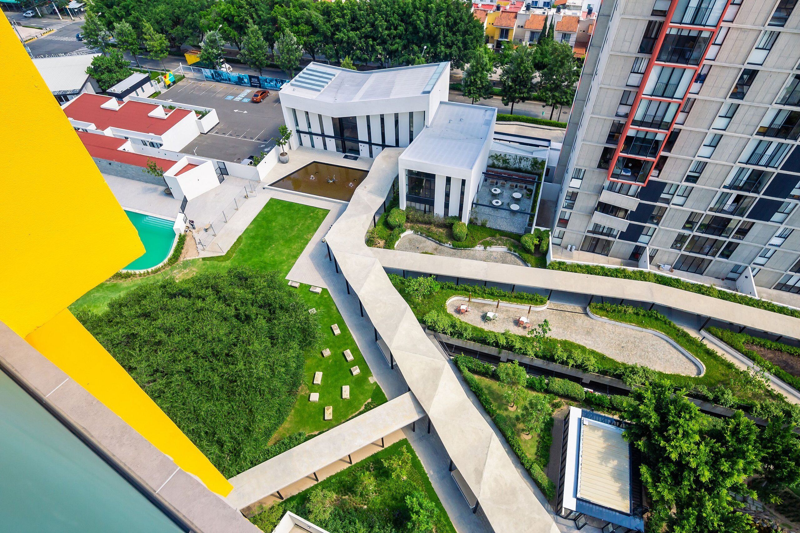 Ein Luftbild eines modernen Gebäudekomplexes mit einem zentralen Innenhof, umliegender Bepflanzung und angrenzenden Hochhäusern.