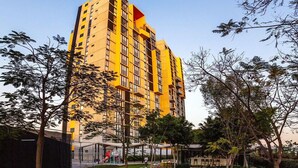 Un hôtel de grande hauteur à la façade jaune, qui se reflète dans une étendue d’eau, et entouré de verdure.