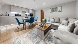Un salon moderne avec un canapé gris, une table basse et des chaises bleues. On y trouve également un coin cuisine avec des meubles blancs et une table à manger.
