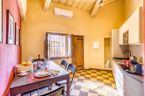 A compact kitchen with a checkered floor, a dining area with a table set for two, and a window with bars. - Romantic Apartment In Chianti Classico (Castelnuovo Berardenga)