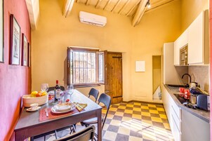 Una cocina compacta con piso a cuadros, una zona de comedor con una mesa lista para dos personas y una ventana con rejas.