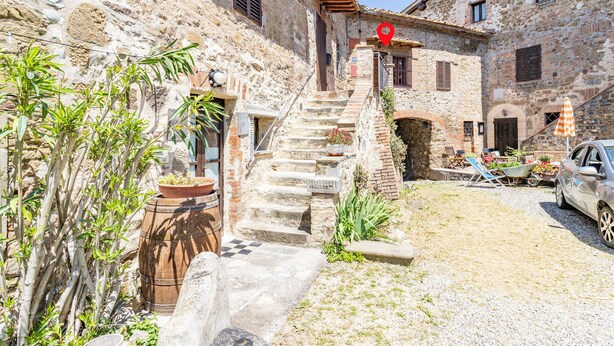 A stone building with a staircase leading to a door, surrounded by plants and a car parked nearby. - Romantic Apartment In Chianti Classico (Castelnuovo Berardenga)