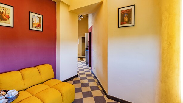 A hotel corridor with a checkered floor, a yellow sofa, and framed pictures on the walls. - Romantic Apartment In Chianti Classico (Castelnuovo Berardenga)