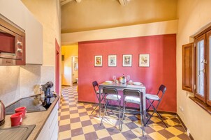 Una cocina con piso a cuadros, una mesa de comedor con sillas y una pared roja con cuadros enmarcados.