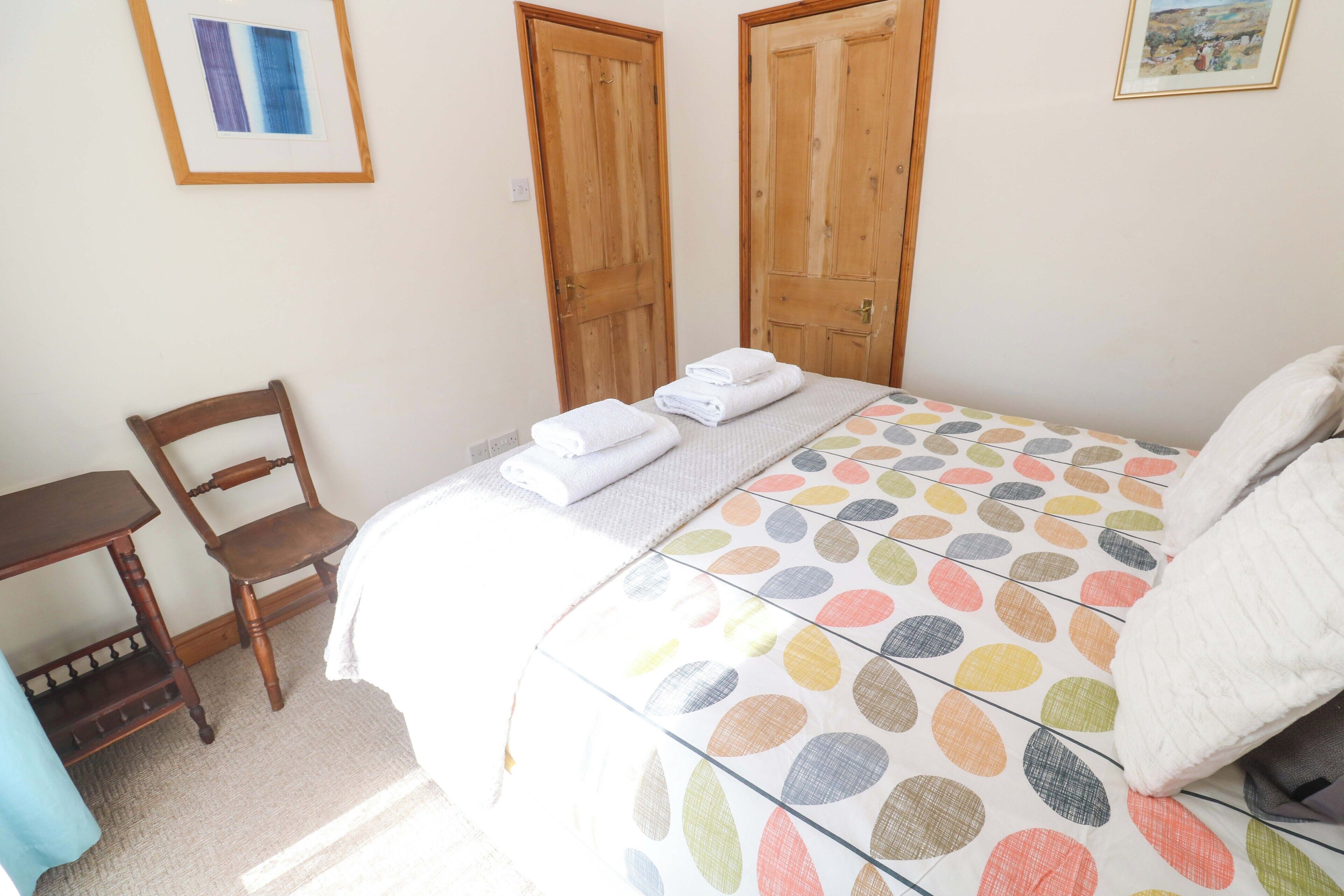 A bedroom with a bed, a chair, a desk, and two wooden doors.