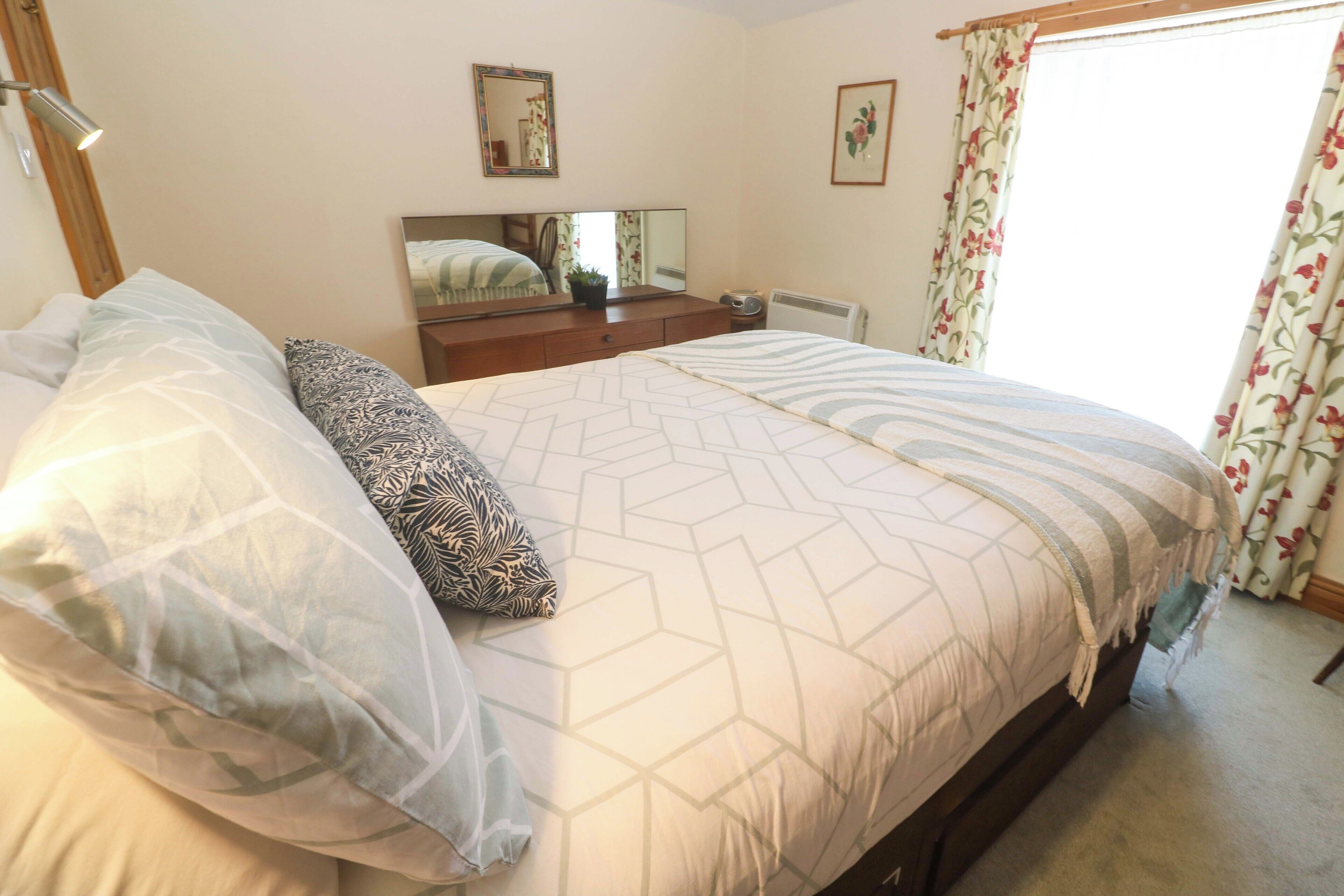 A bedroom with a bed, a dresser, a mirror, and a window with curtains.