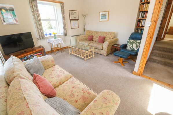 A living room with a sofa, a chair, a glass coffee table, a television, and a bookshelf.