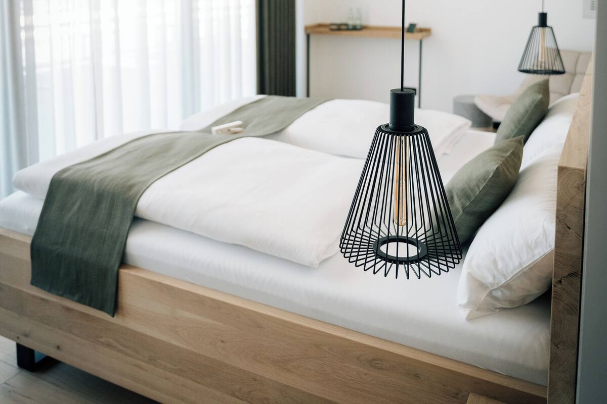 A modern bedroom with a wooden bed, white bedding, and two hanging pendant lights.