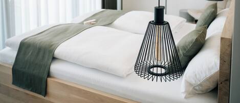 Een moderne slaapkamer met een houten bed, witte beddengoed en twee hangende pendellampen.