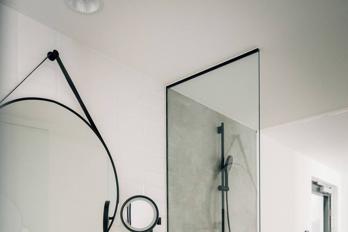A modern bathroom with a glass-enclosed shower, a wooden vanity with a white sink, and a round mirror.