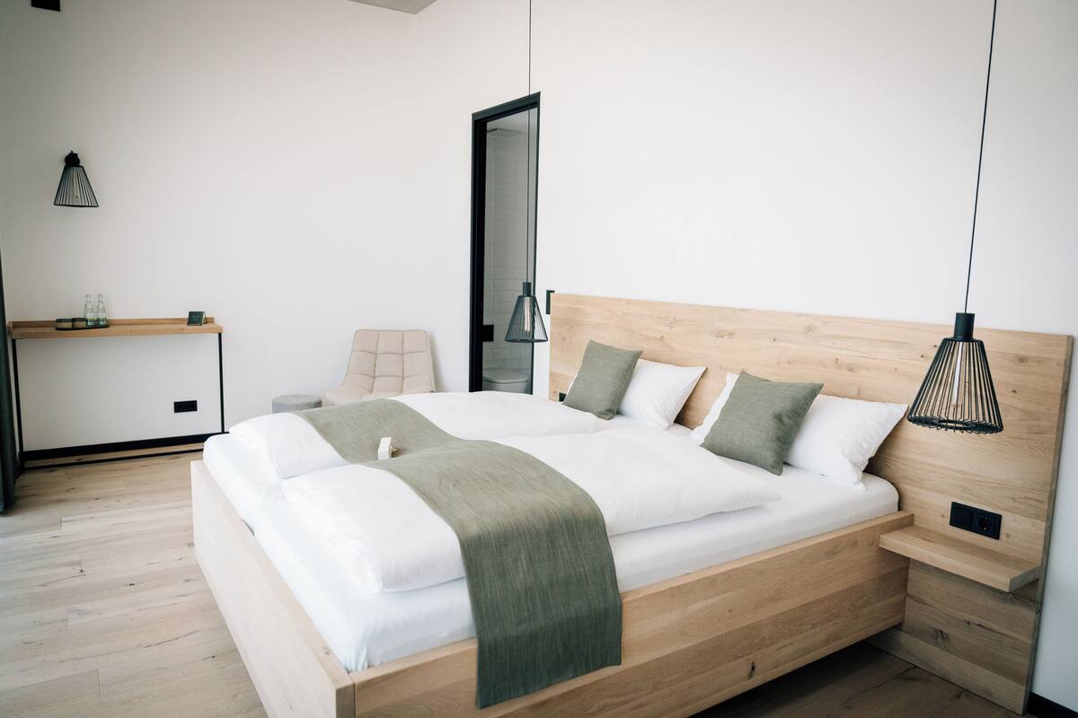 A modern bedroom with a wooden bed, bedside tables, a nightstand, a bench, and a hanging lamp.