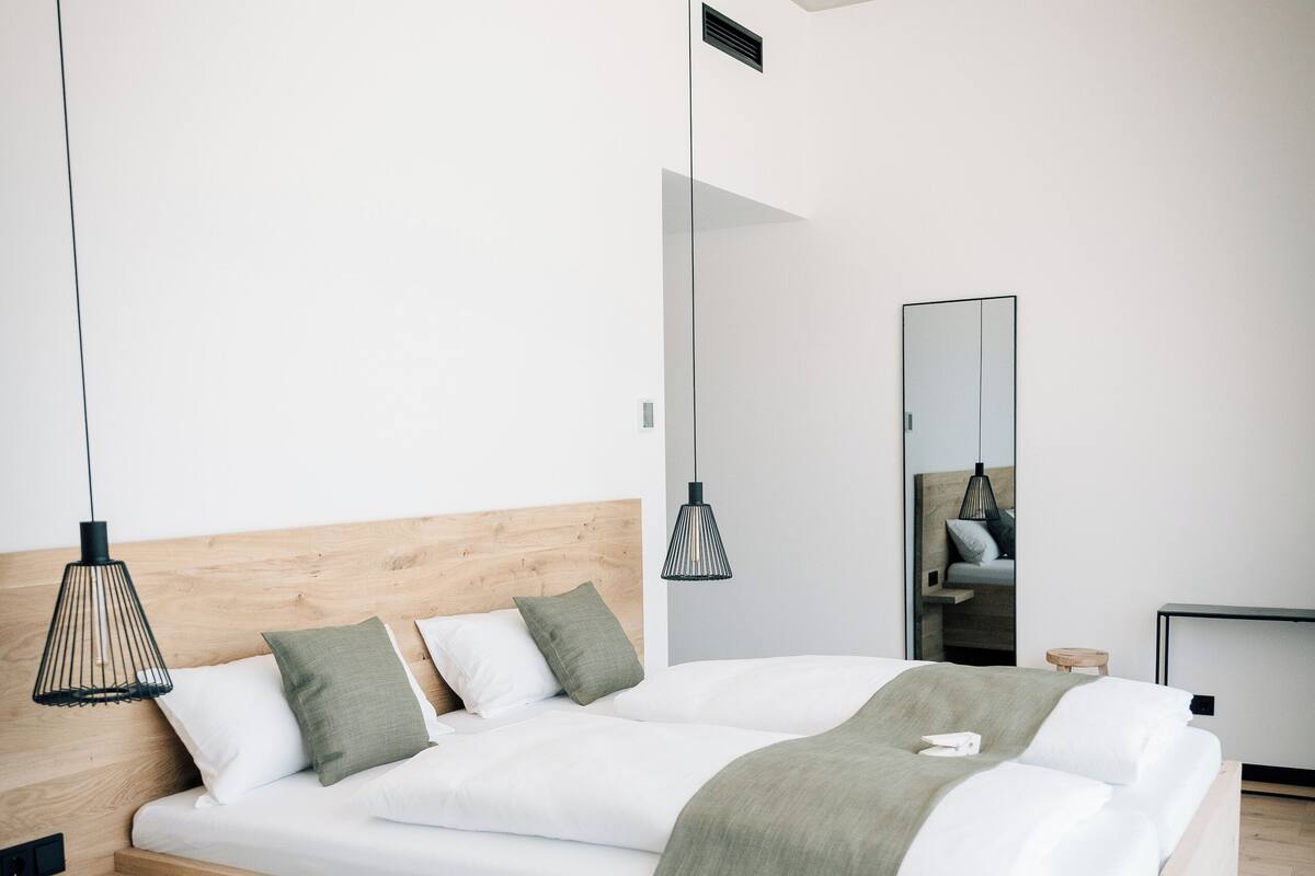 A modern bedroom with a wooden bed, two bedside tables, a nightstand, a mirror, and pendant lights.