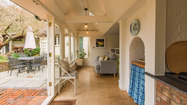 A covered patio area with a dining table and chairs, a cushioned bench, and a fireplace. - Water Farm House, Stowting (Stowting)
