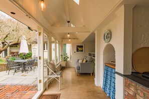 A covered patio area with a dining table and chairs, a cushioned bench, and a fireplace. - Water Farm House, Stowting (Stowting)