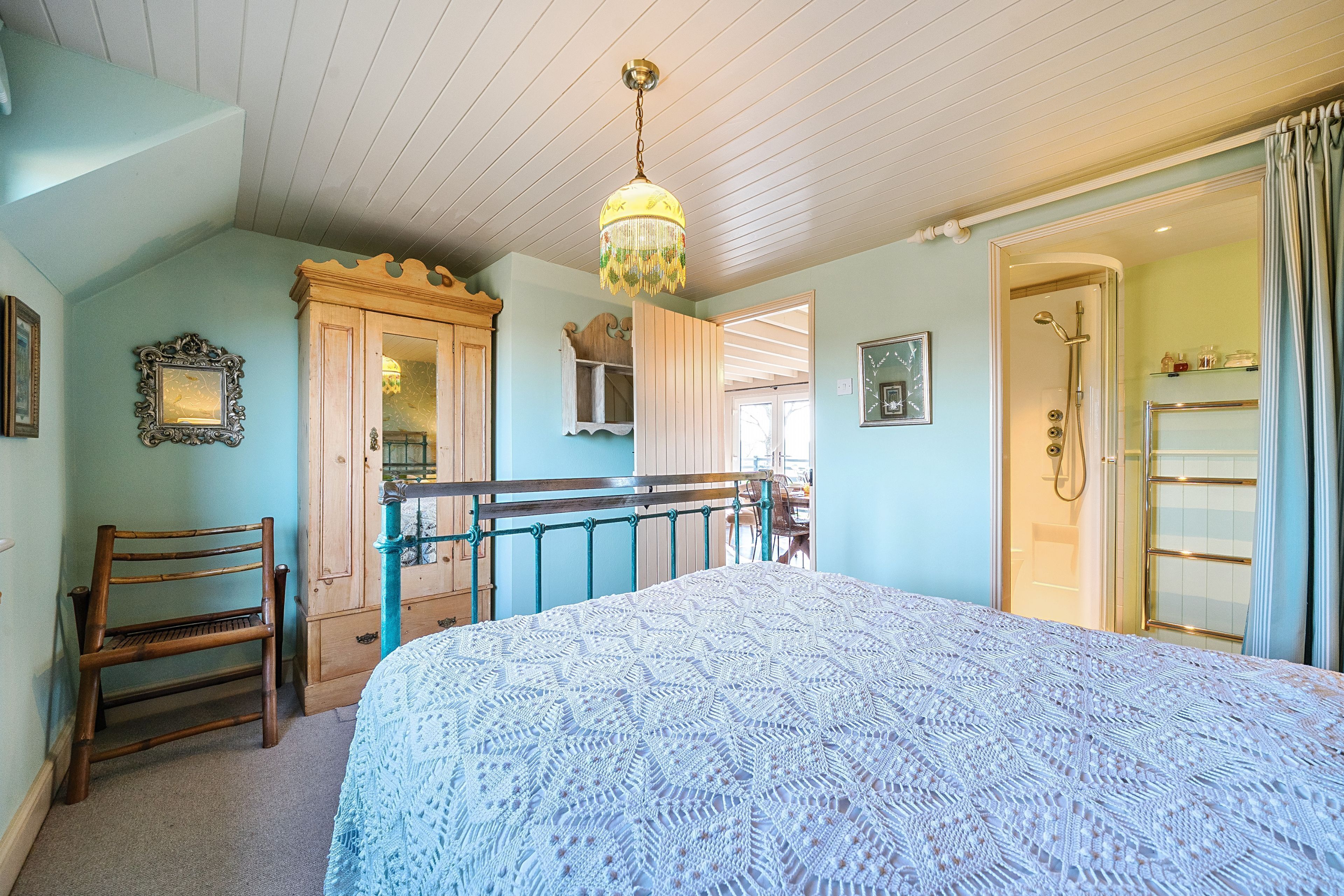 Une chambre avec un grand lit, une chaise en bois, une commode et un espace douche.