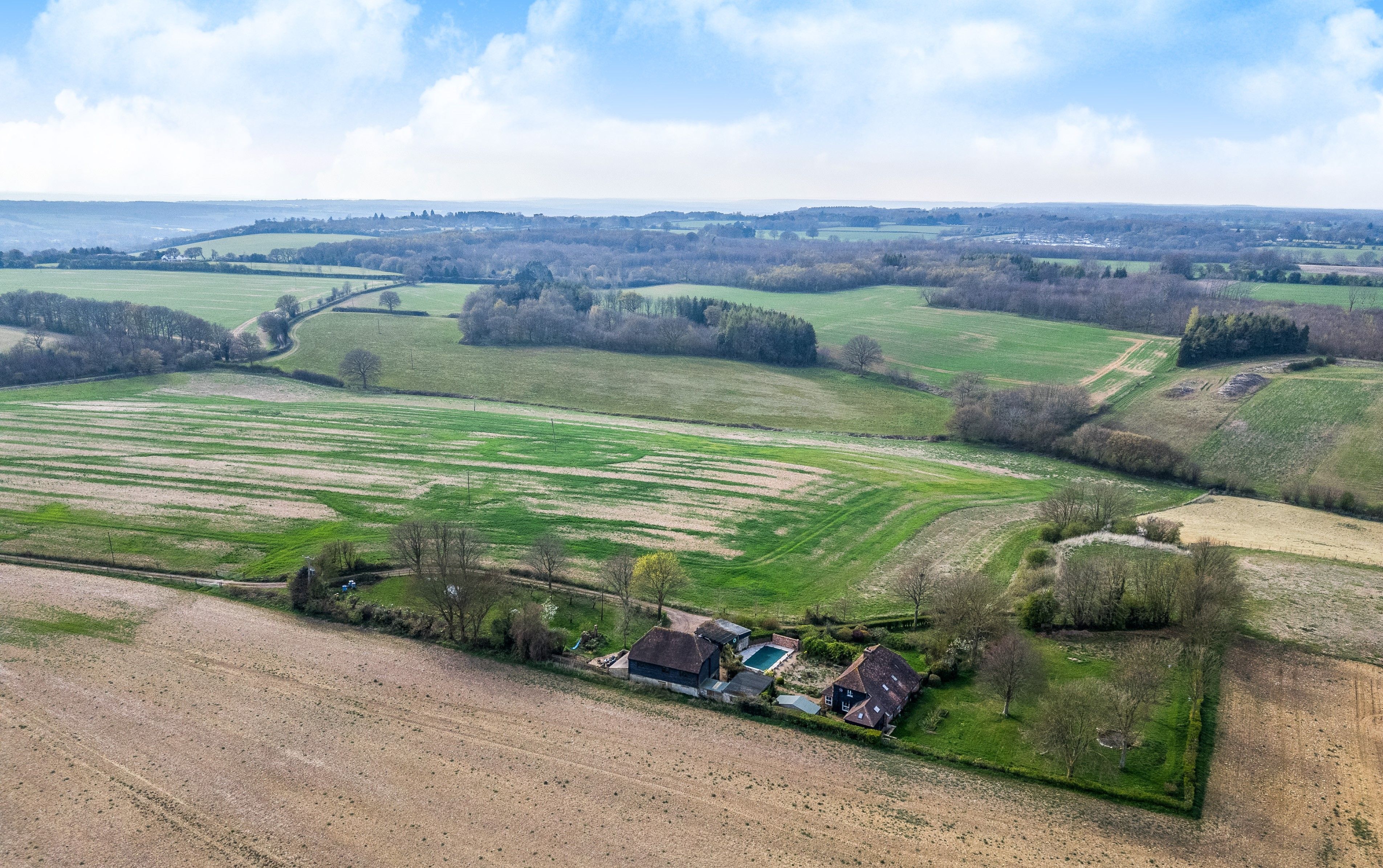 An aerial view of a rural property with fields, a farmhouse, and a swimming pool.