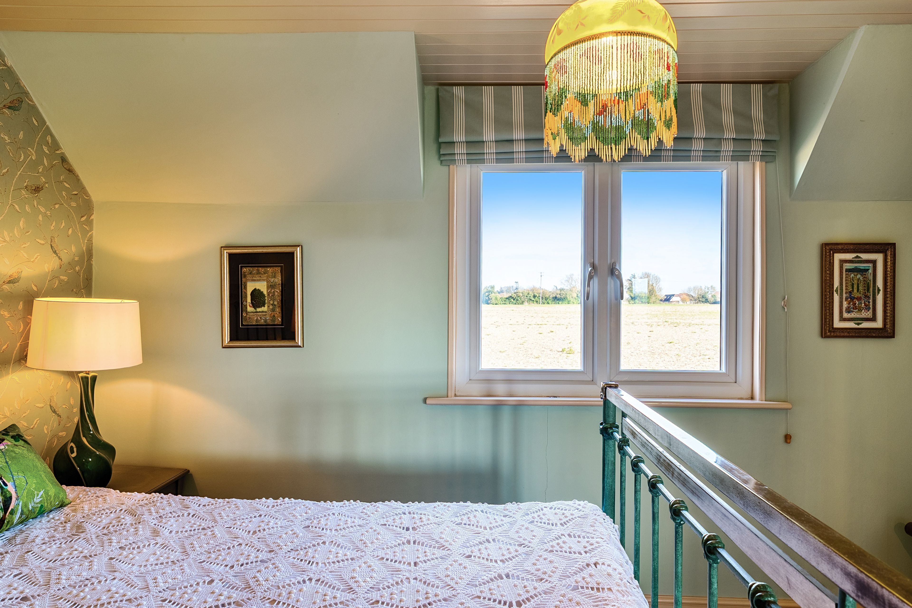 Quarto com uma cama, janela com vista, abajur e quadros na parede.