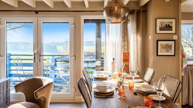 Comedor con mesa de madera dispuesta para cuatro personas, sillas e iluminación colgante.