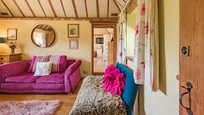 A cozy room with a wooden ceiling, a purple sofa, a blue headboard, and a fluffy rug. - Pond Cottage, Egerton (Egerton)