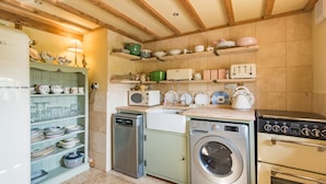 A kitchen with a dishwasher, washing machine, and oven. There are shelves with dishes and a microwave. - Pond Cottage, Egerton (Egerton)