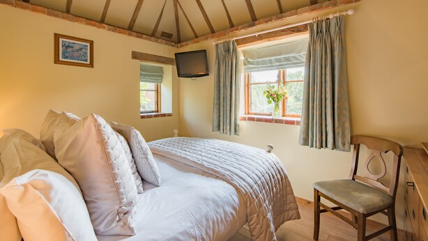 A bedroom with a bed, a chair, a television, and a window with curtains. - Pond Cottage, Egerton (Egerton)