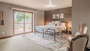 Een slaapkamer met een bed, nachtkastje, stoel, groot raam en een houten wand.