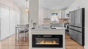 A modern kitchen with a built-in fireplace, stainless steel appliances, and a dining area with a white table and chairs. - MINNeSTAY* Meadows Retreat (Saint Michael)