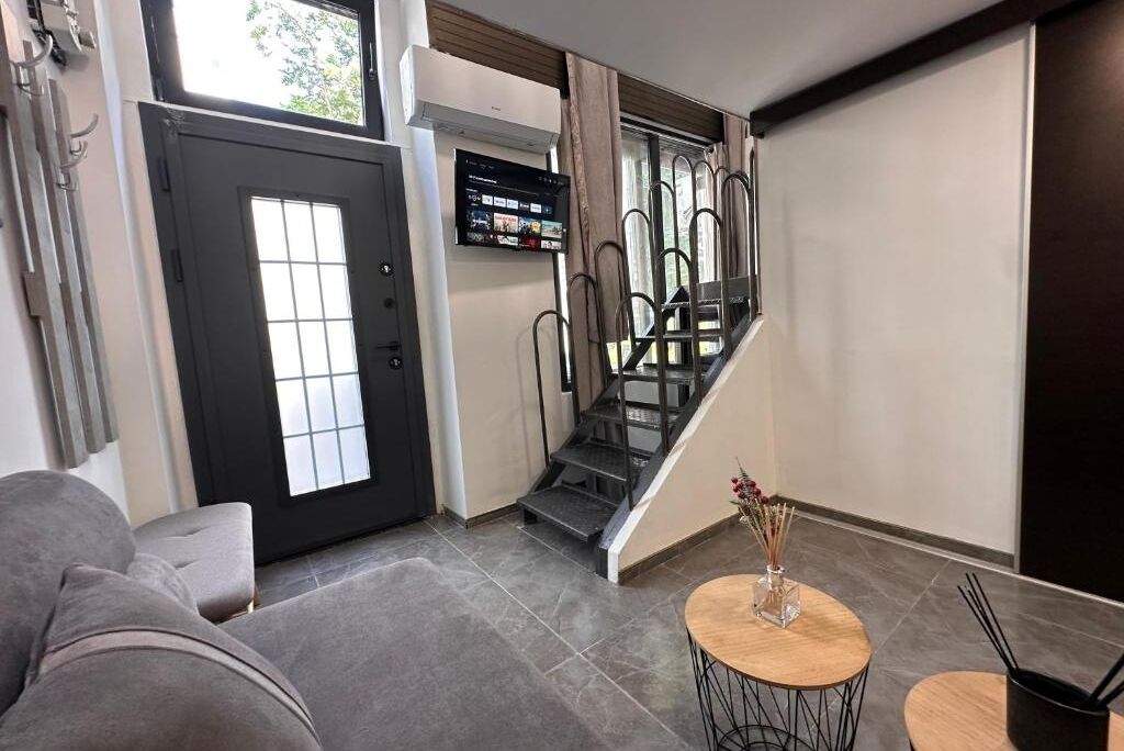 A modern living room with a grey sofa, a small round table with a vase, and a staircase leading to a balcony.
