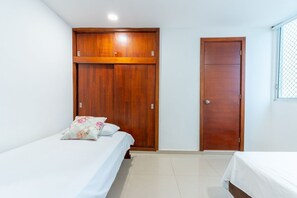 Une chambre avec deux lits, des armoires en bois et une fenêtre munie d’un moustiquaire.