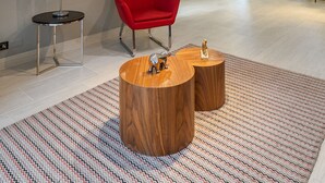 Una sala de estar moderna con una silla roja, dos mesas de centro de madera y un televisor montado en la pared.