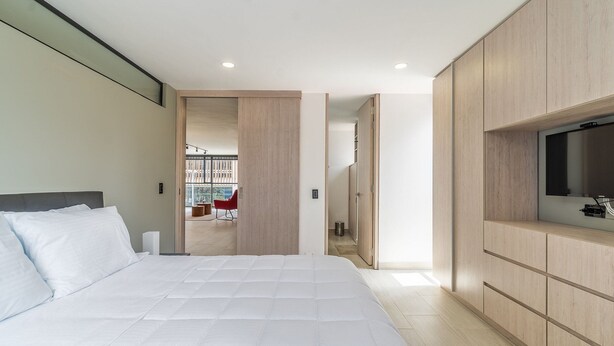 Un dormitorio moderno con una cama grande, armario de madera empotrado y televisor.