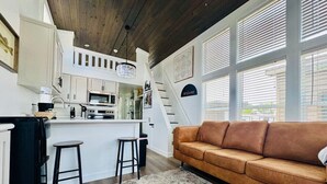 A modern kitchen with white cabinets, a central island, and a staircase leading to an upper level. - The Little Lonestar with Pool & Hot Tub (Austin)