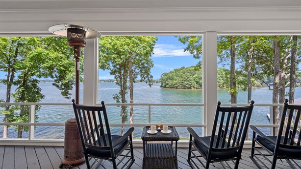 A wooden deck with rocking chairs and a table with cups and saucers, overlooking a lake with trees and a clear sky. - Blissfully Together- Blue Heron + Back Porch Sleeps 22 (Mooresville)