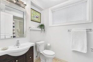Een badkamer met een witte wastafel, een donker houten wastafelmeubel, een wit toilet en een raam met zonwering.