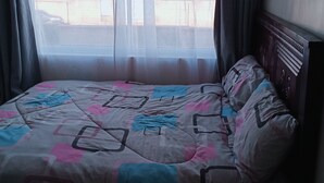 A bed with a geometric patterned bedspread, a wooden headboard, and a window with sheer curtains. - 5 minutes to Ngong hills! Family-sized condo with gym , supermarket $ school (Nairobi)