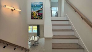 A modern staircase with wooden steps and white railings, leading to a dining area with a table and chairs. - Art Deco~Miami~Jacuzzi~Game Room~2 min. to Beach! (Panama City Beach)