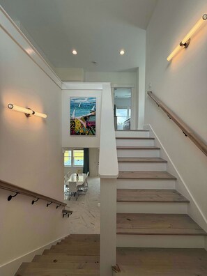 Eine moderne Treppe mit Holzstufen und weißen Geländern, die zu einem Essbereich mit Tisch und Stühlen führt.