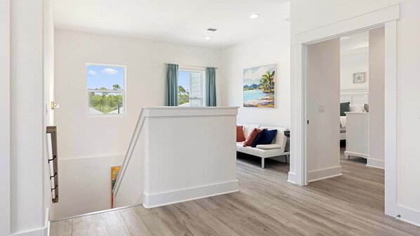 A modern interior with a staircase leading to a living area, a painting of a beach scene, and a clock on the wall. - Art Deco~Miami~Jacuzzi~Game Room~2 min. to Beach! (Panama City Beach)