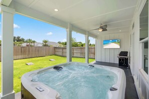 Ein Whirlpool in einem überdachten Außenbereich mit Holzzaun und Rasen im Hintergrund.