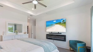 A bedroom with a large bed, a television mounted on the wall, a mirror, and a teal chair. - Art Deco~Miami~Jacuzzi~Game Room~2 min. to Beach! (Panama City Beach)