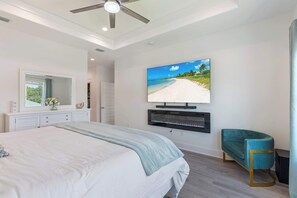 Ein Schlafzimmer mit einem großen Bett, einem an der Wand befestigten Fernseher, einem Spiegel und einem Türkissessel.